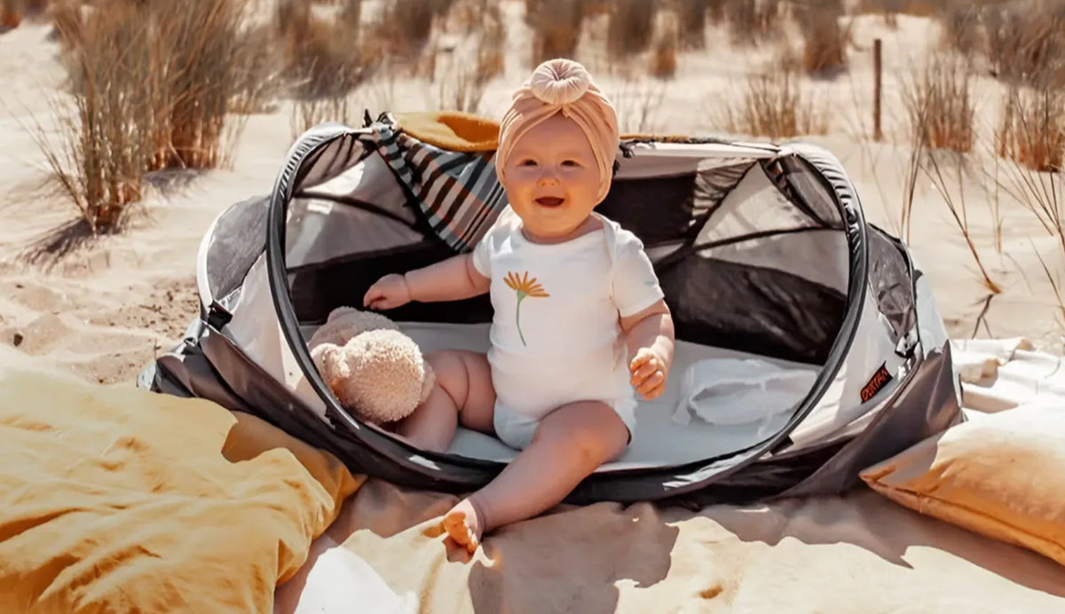 Baby in een DERYAN reistentje op het strand